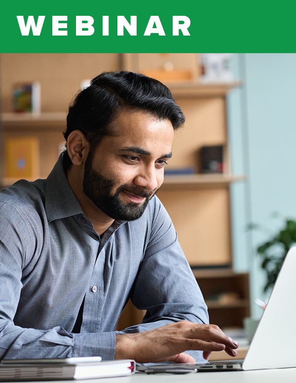 A bearded man smiling while working on his laptop.